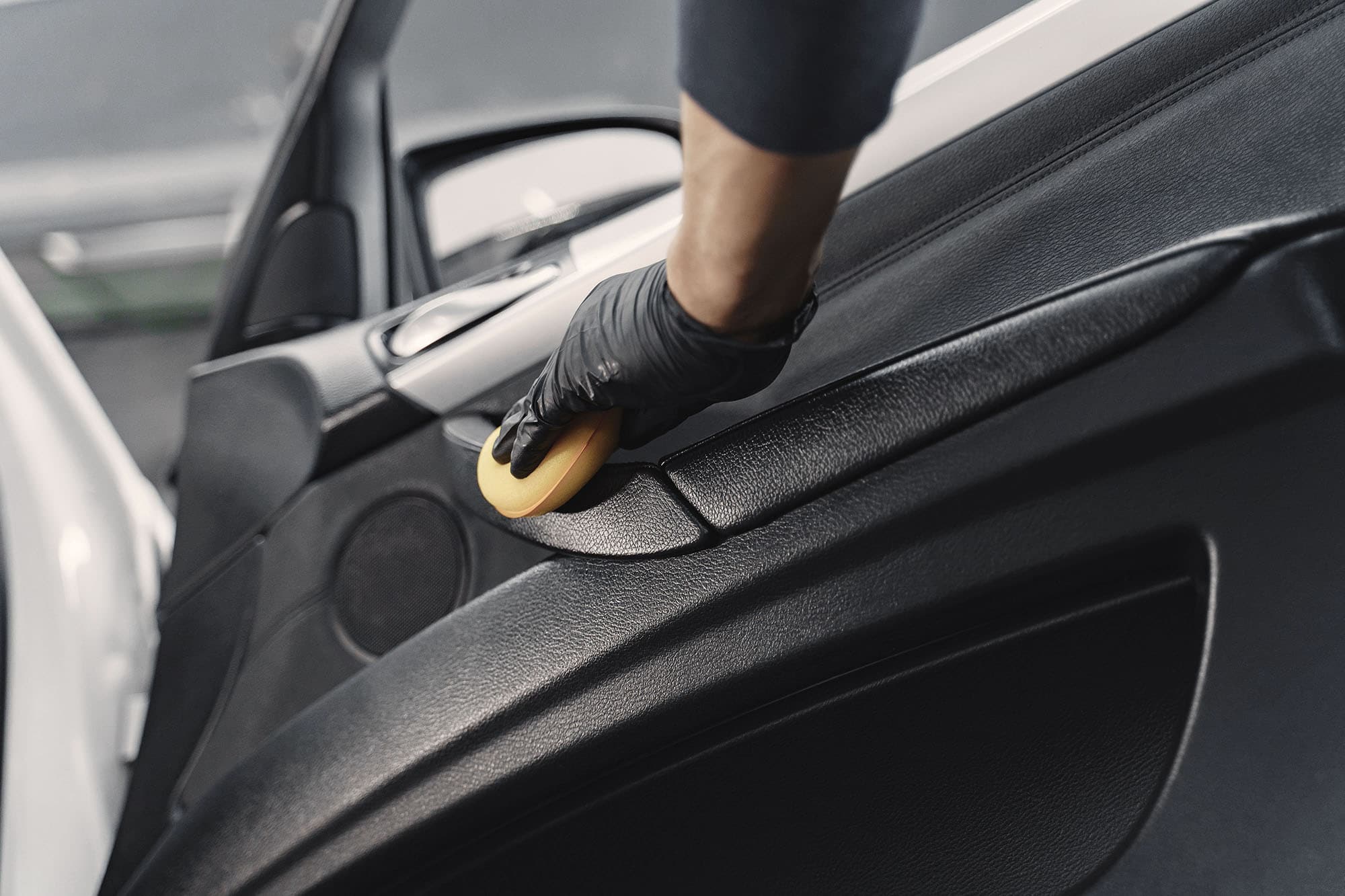 Detailer cleaning and polishing the car door interior as part of a professional interior car detailing service.